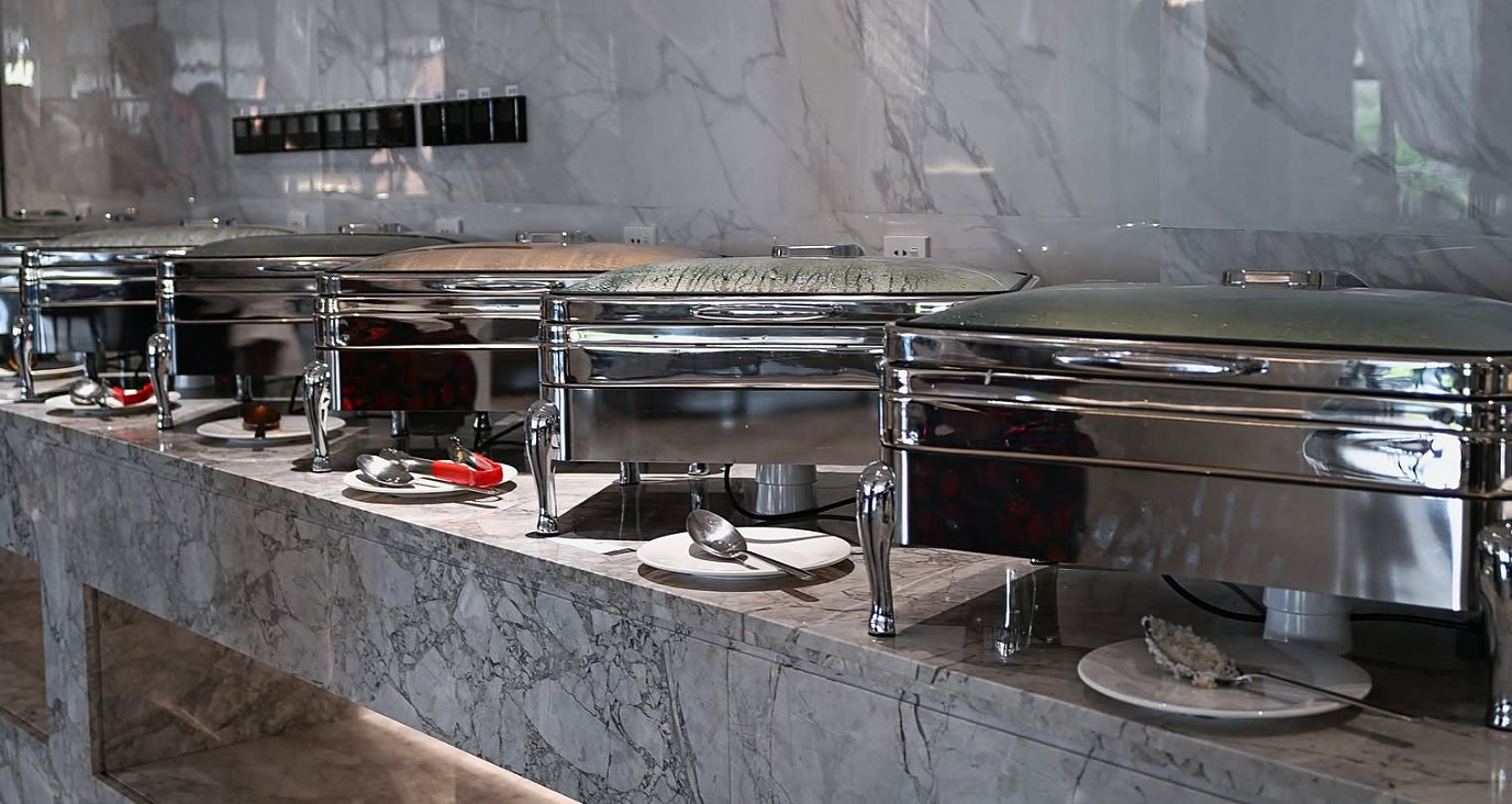 Stainless-steel chafing dishes along a marble buffet counter